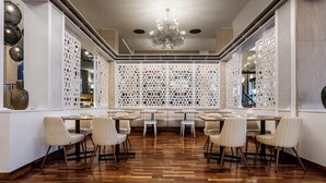 A restaurant with wooden flooring, white chairs, and a decorative white partition with geometric patterns.