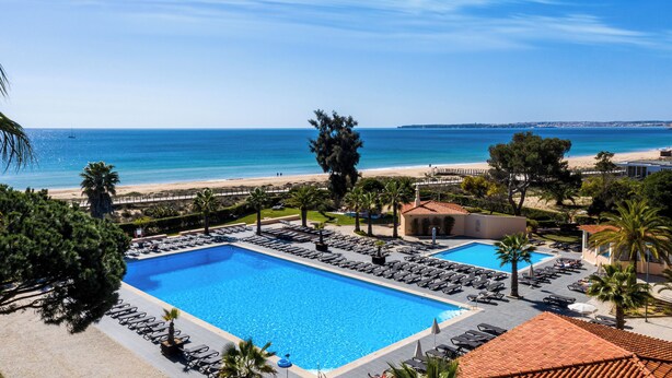A resort with a large swimming pool, sun loungers, and a view of the beach and ocean.