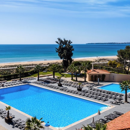 A resort with a large swimming pool, sun loungers, and a view of the beach and ocean.