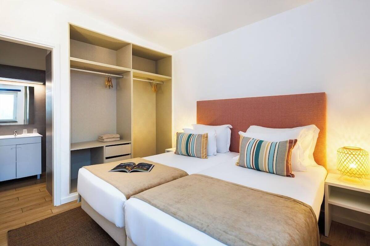 A hotel room with two beds, a walk-in closet, a bathroom, and a bedside lamp.