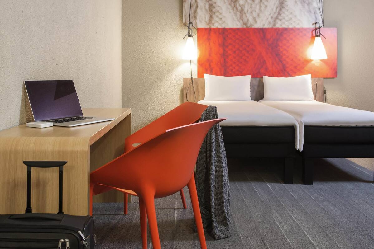 A hotel room with a bed, desk, chair, and a suitcase.