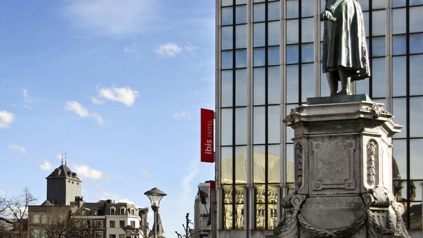 A statue in front of a modern building with a red banner. - ibis Liège Centre Opéra (Liege)