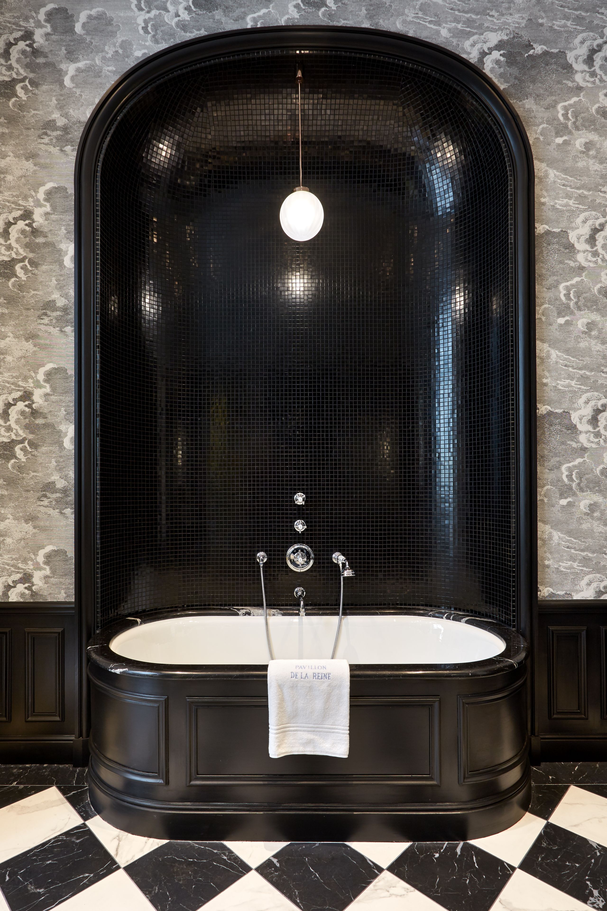 Eine schwarze Badewanne mit einem weißen Handtuch, einer hängenden Lampenleuchte und einer strukturierten Wand dahinter.