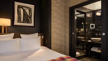 Une chambre d’hôtel comprenant un lit, un grand miroir, une salle de bain avec un lavabo et un miroir, et une œuvre d’art encadrée accrochée au mur.