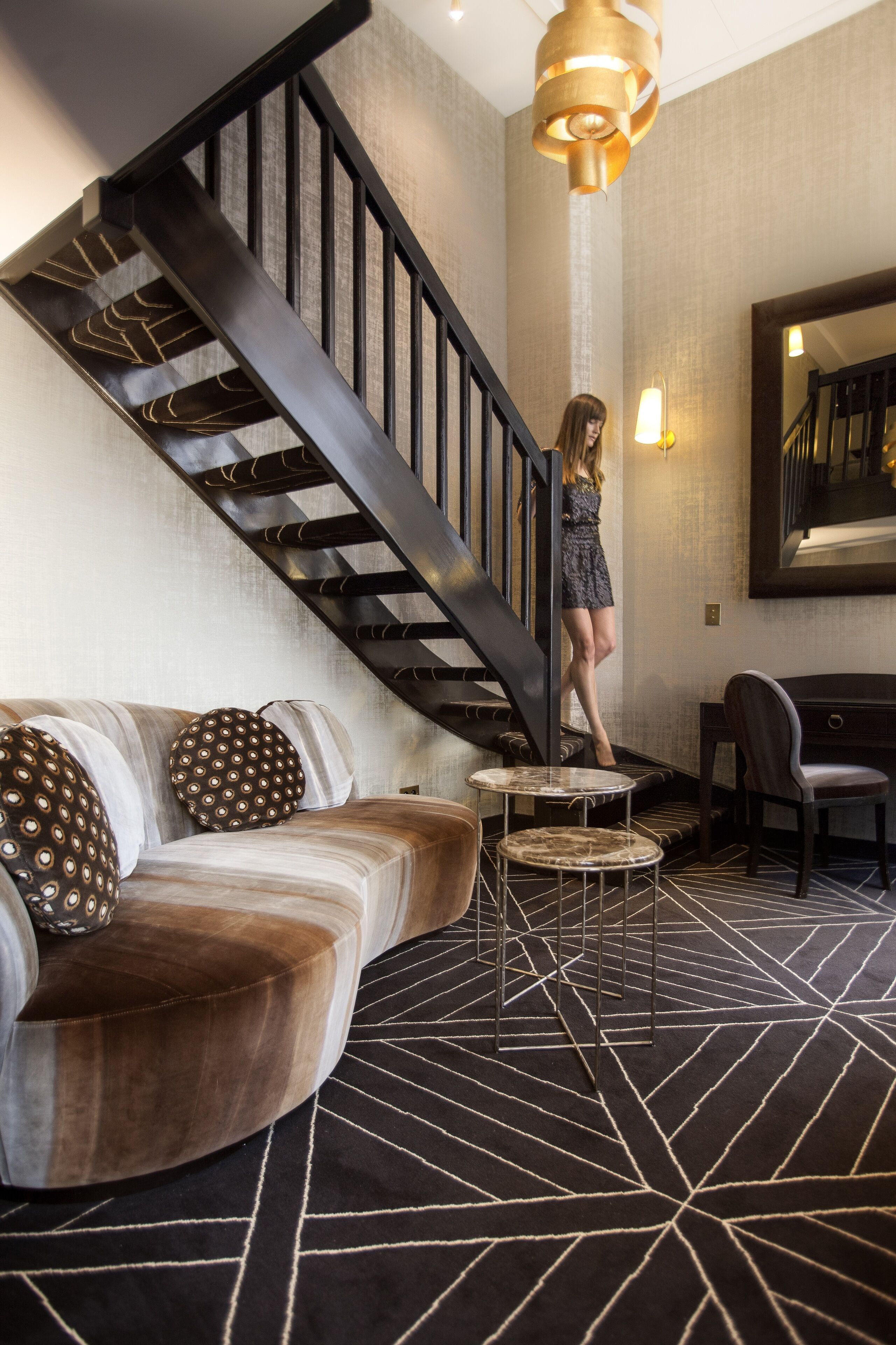 Un interior moderno con una escalera, un sofá con cojines estampados, una mesa redonda y una silla.