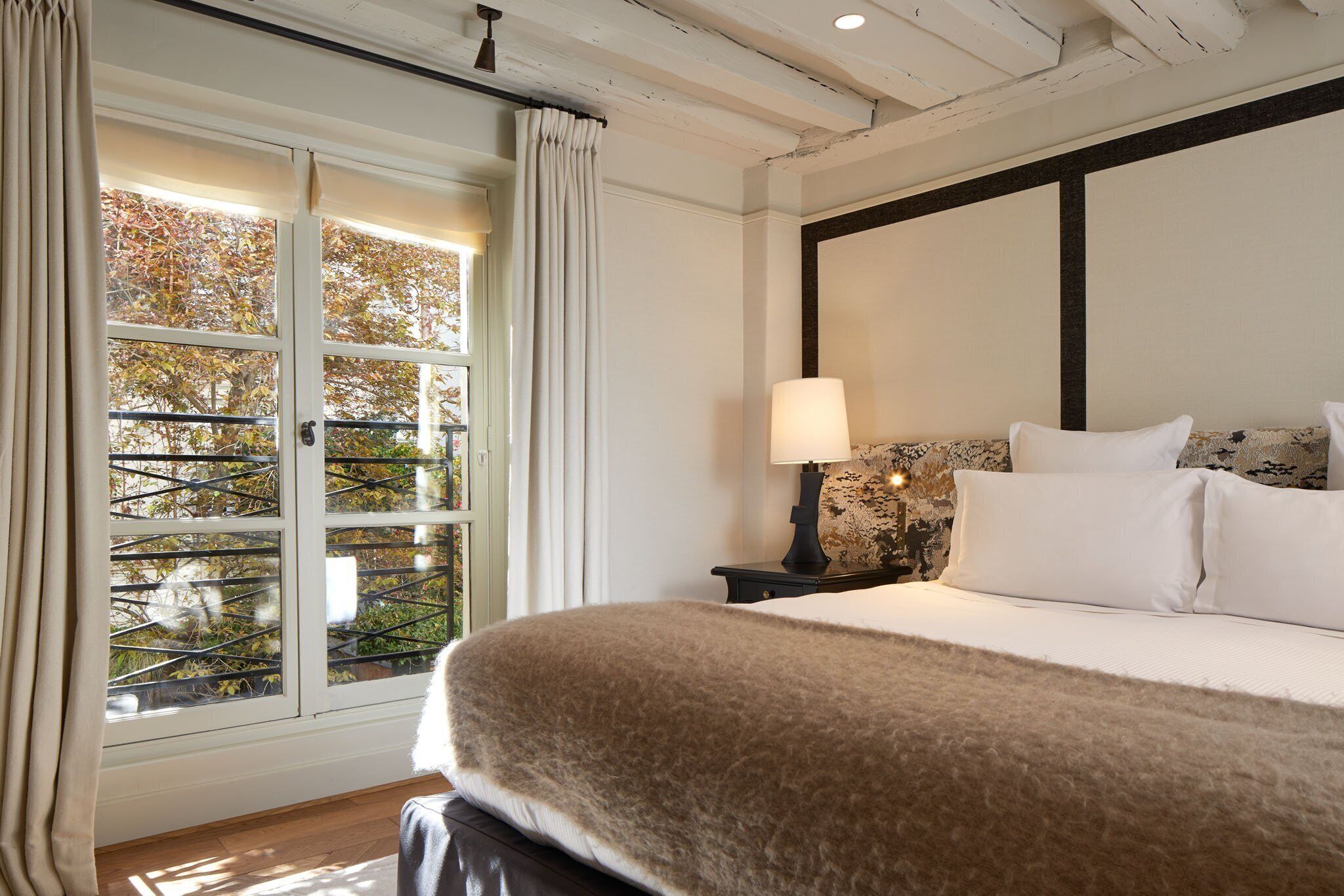 A bedroom with a large bed, a nightstand with a lamp, and a window with curtains.