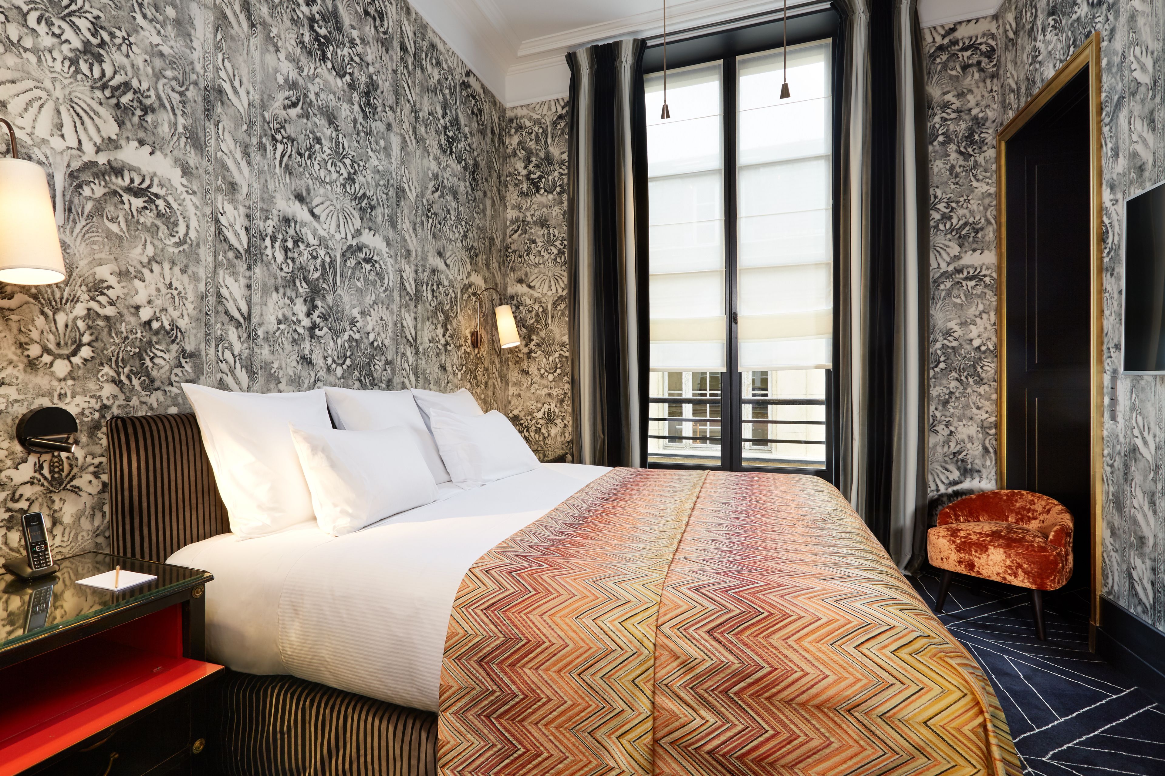 A hotel room with a large bed, a red nightstand, a telephone, and a chair.