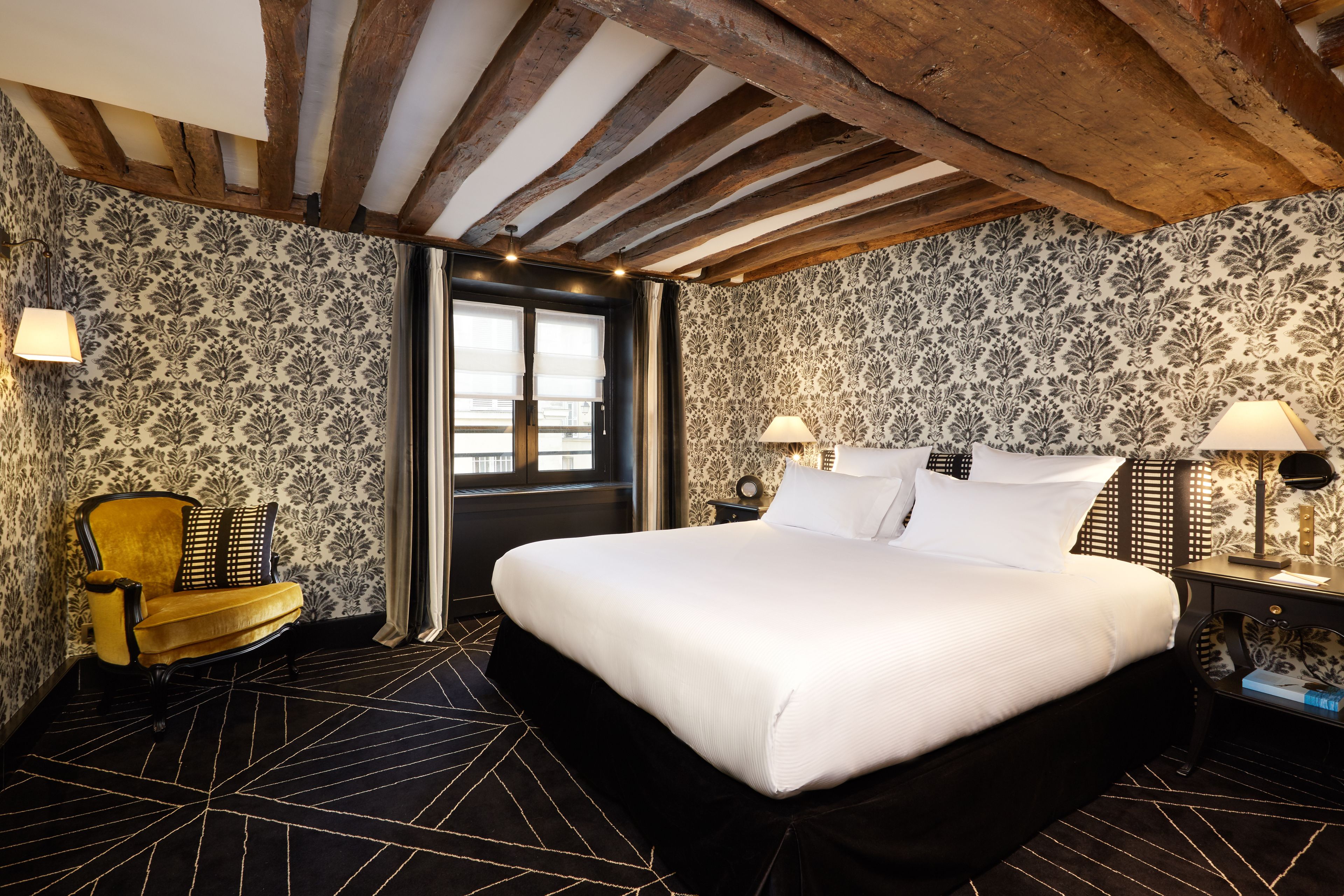 Quarto de hotel com uma cama grande, uma cadeira e uma mesa de cabeceira com luminárias.
