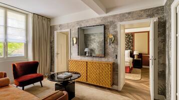 A hotel room with a modern design, featuring a red chair, a round coffee table, a yellow patterned console, and a large mirror on the wall.