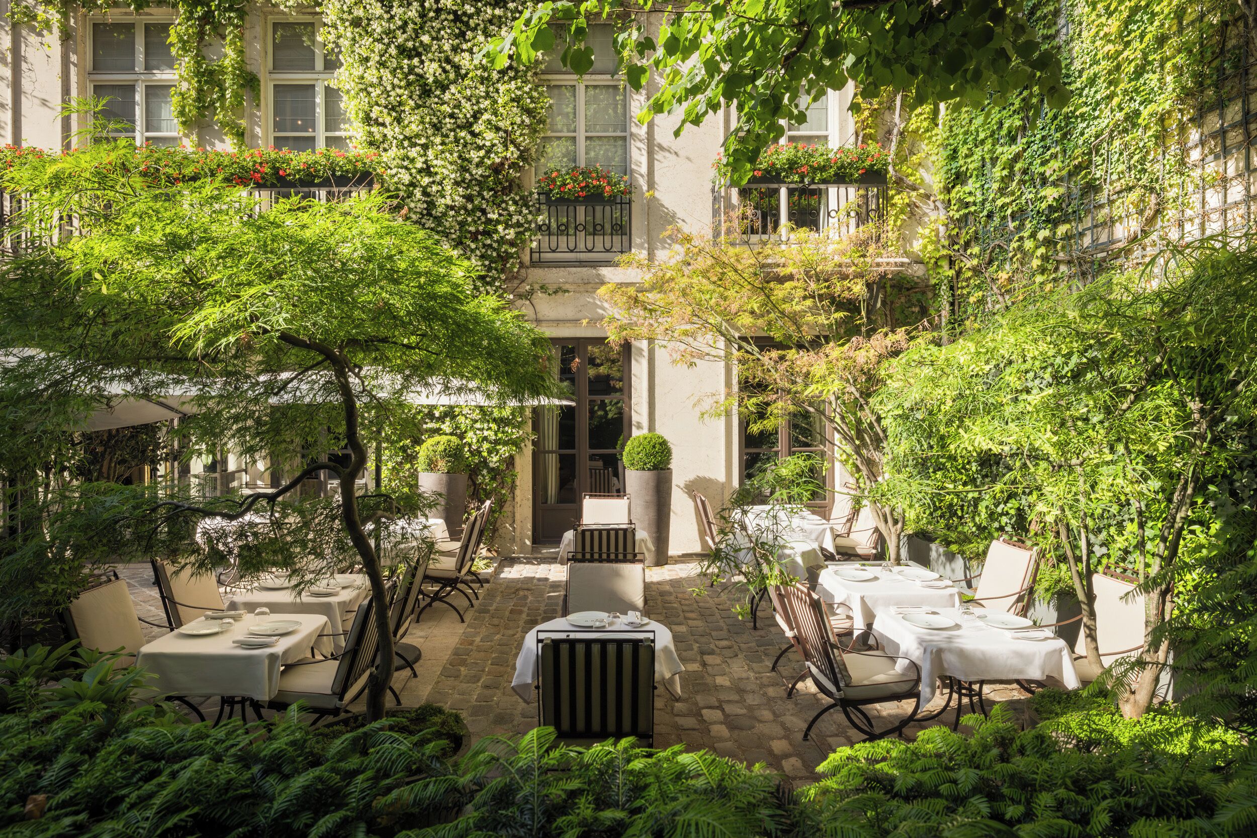 A courtyard with outdoor seating, surrounded by lush greenery and a building with multiple windows and balconies.