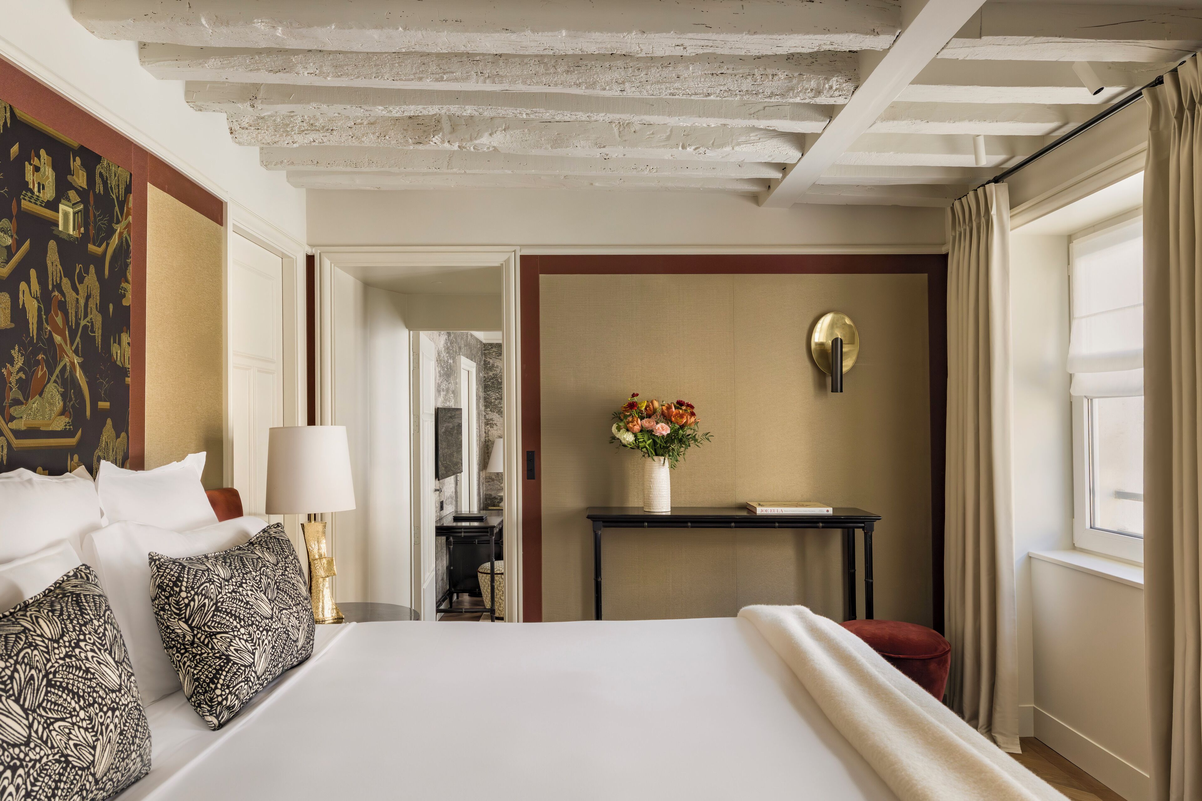 A hotel room with a large bed, a desk, a vase with flowers, and a view of the outside.