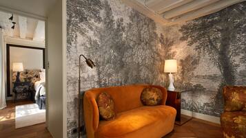A room with a large mural of trees on the wall, a sofa with two decorative pillows, a floor lamp, and a small table with a lamp.
