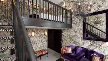 A room with a black staircase, a purple sofa, patterned cushions, and a chandelier.