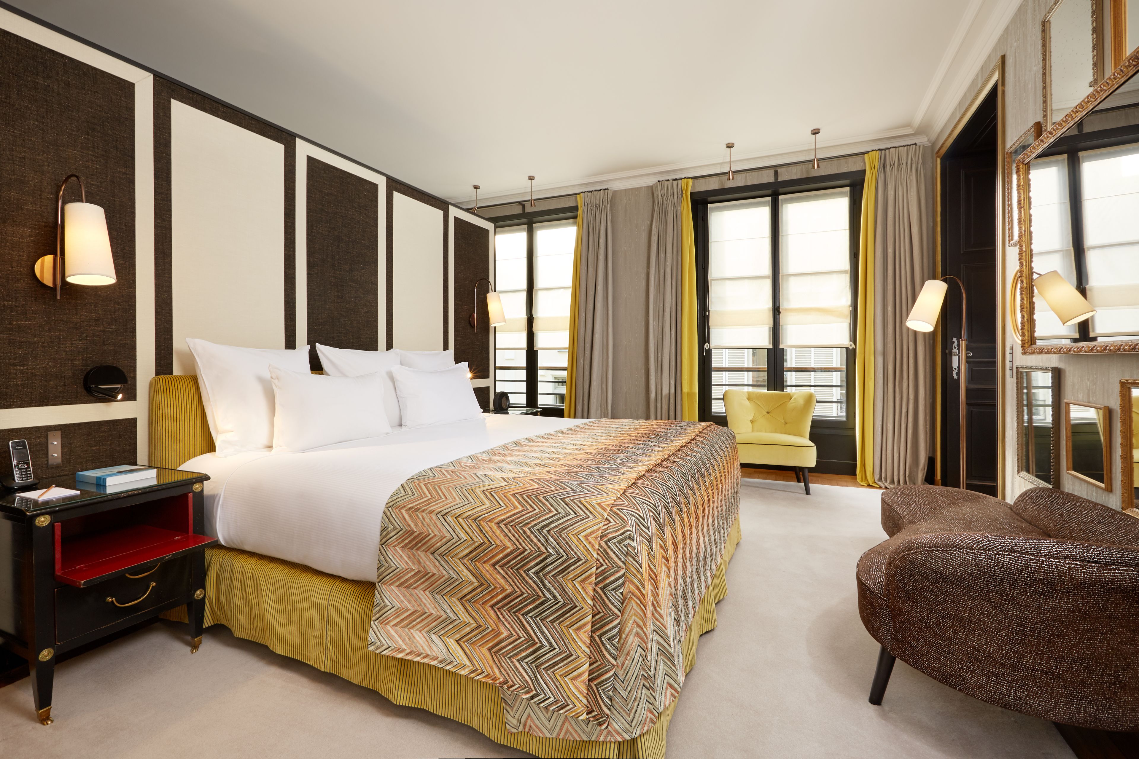 A hotel room with a large bed, a nightstand, a chair, and a large window with curtains.