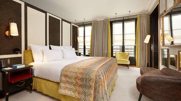 A hotel room with a large bed, a nightstand, a chair, and a large window with curtains.