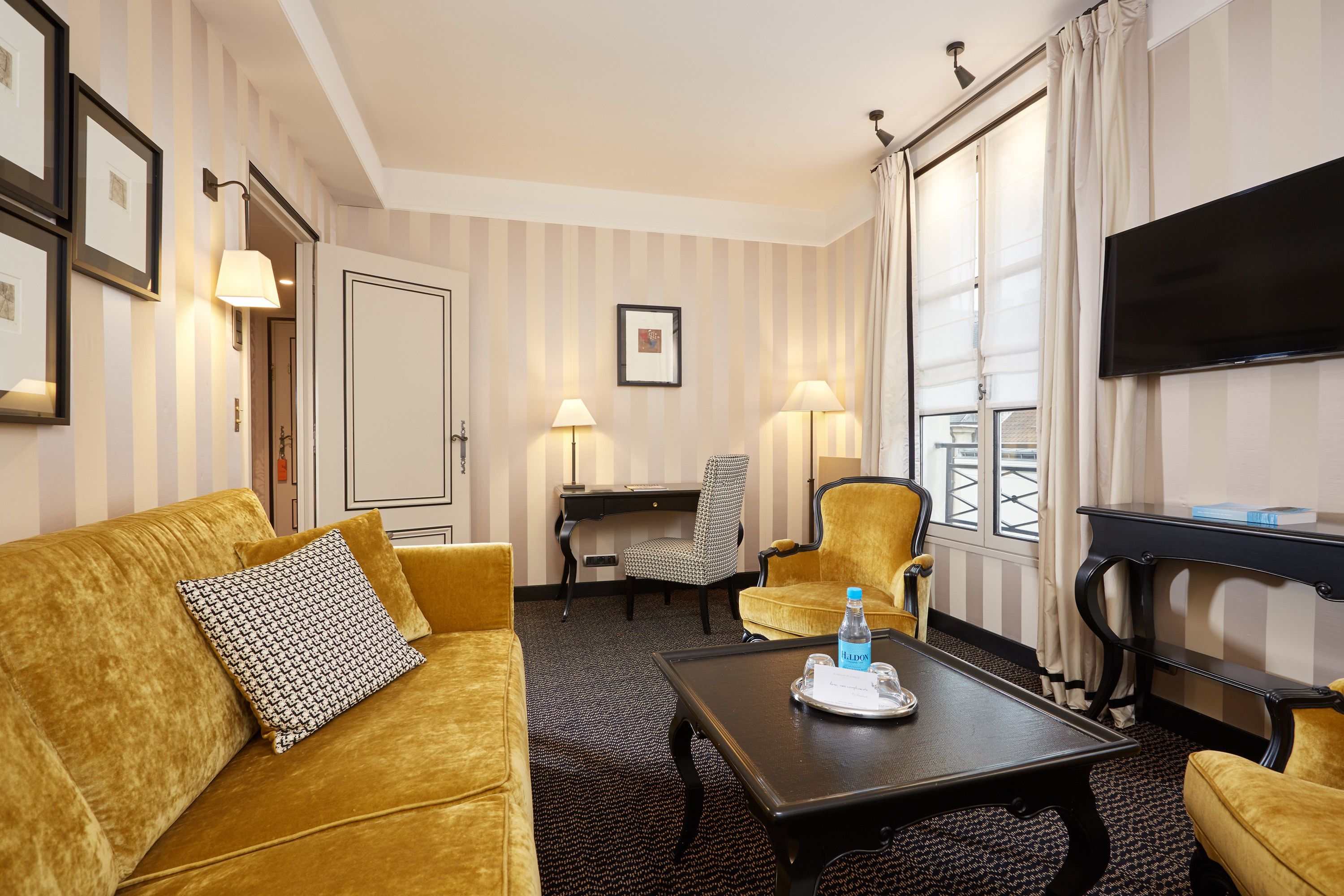 A hotel room with a sofa, two armchairs, a desk, a television, and a window with curtains.