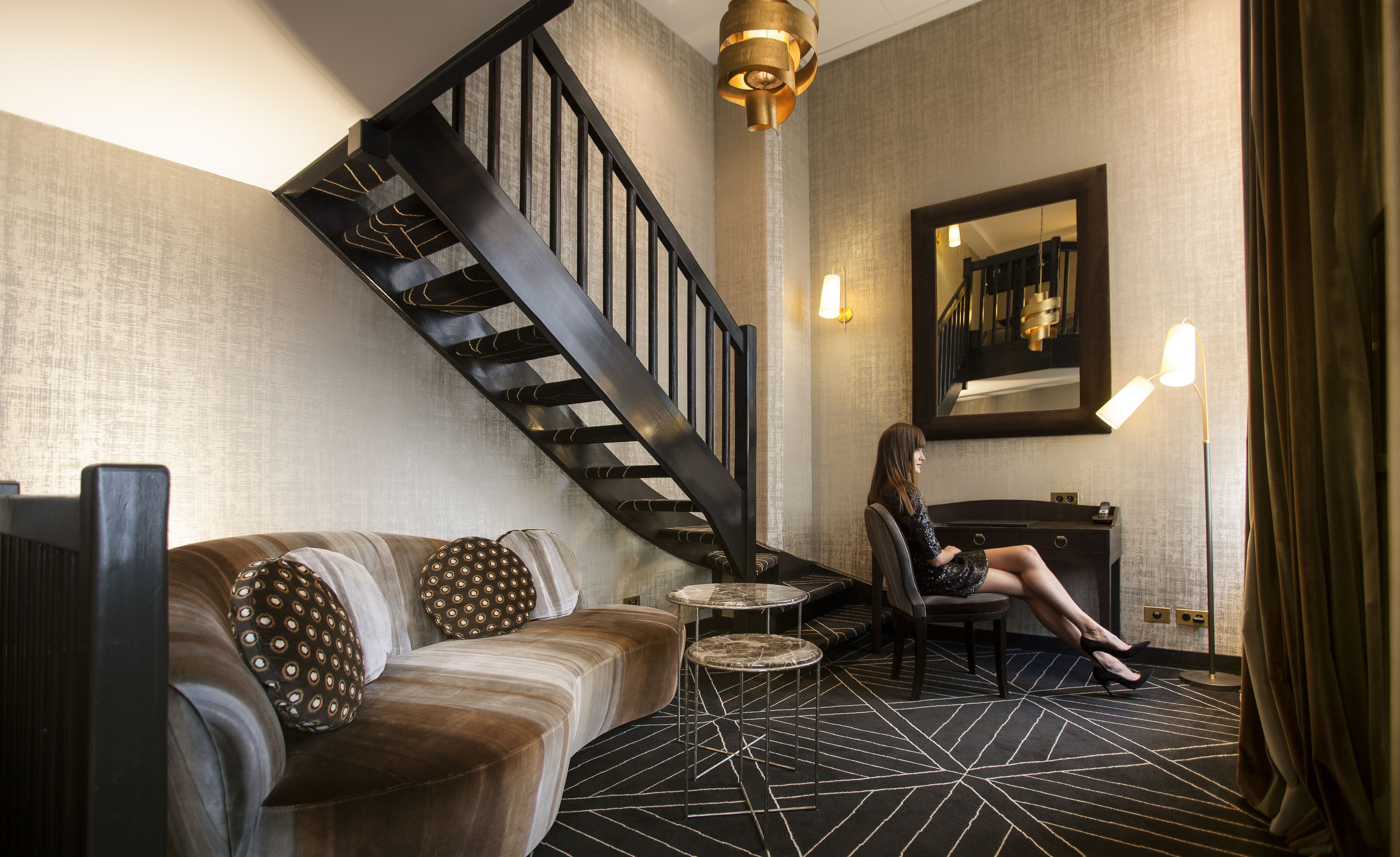 A modern interior with a curved sofa, a small round table, a chair, a staircase, and a large mirror on the wall.
