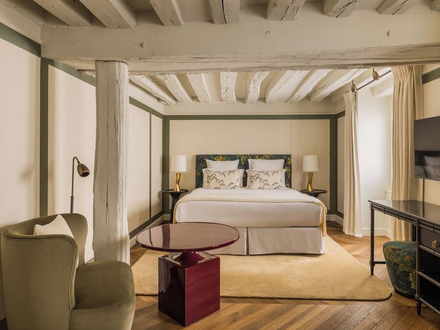 A bedroom with a bed, bedside tables, a chair, a small table, and a TV.