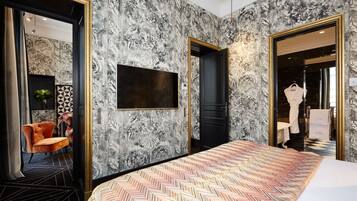 A hotel room with a large bed, a TV mounted on the wall, and a wardrobe with a mirror.