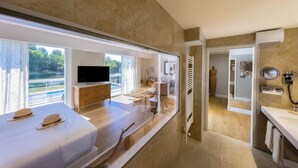 A modern hotel room with a large window, a flat-screen TV, a wooden dresser, a vanity with a mirror, and a bathroom visible through an open door. - La Réserve Albi - Hotel Restaurant (Albi)