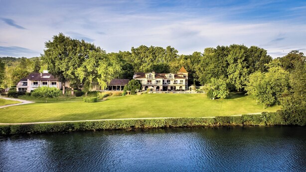 A large, multi-story house with a well-maintained lawn and a body of water in the foreground. - La Réserve Albi - Hotel Restaurant (Albi)