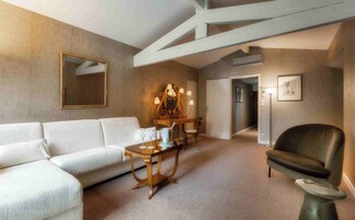 Una sala moderna con un sofá blanco, una mesa de centro de madera, un sillón oscuro y una lámpara de pie. Hay un espejo con un marco decorativo y un candelabro en la pared.