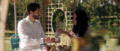 A couple dining at an outdoor table with a garden view, surrounded by a lattice structure.