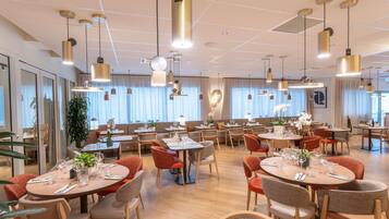 Ein modernes Restaurant mit mehreren Essbereichen, darunter Sitzecken und Tische mit Stühlen.