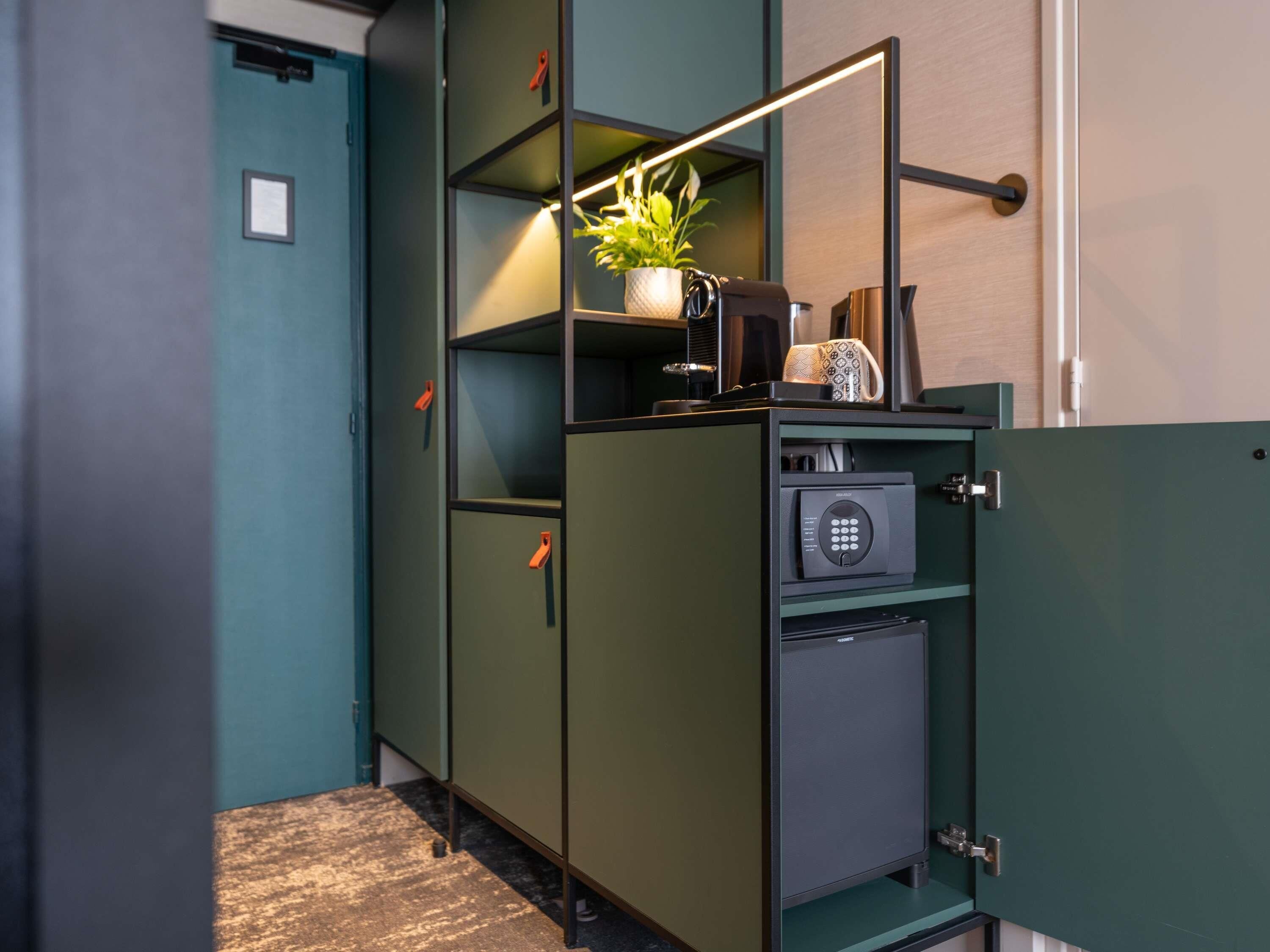 A compact, modern room with a teal door, a small kitchenette area, and a built-in safe.