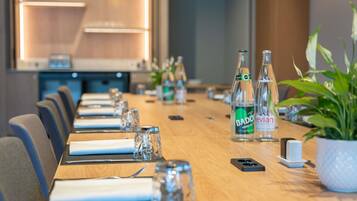 Een vergaderzaal met een lange tafel gedekt voor een vergadering, voorzien van glazen, waterflesjes en een potplant.