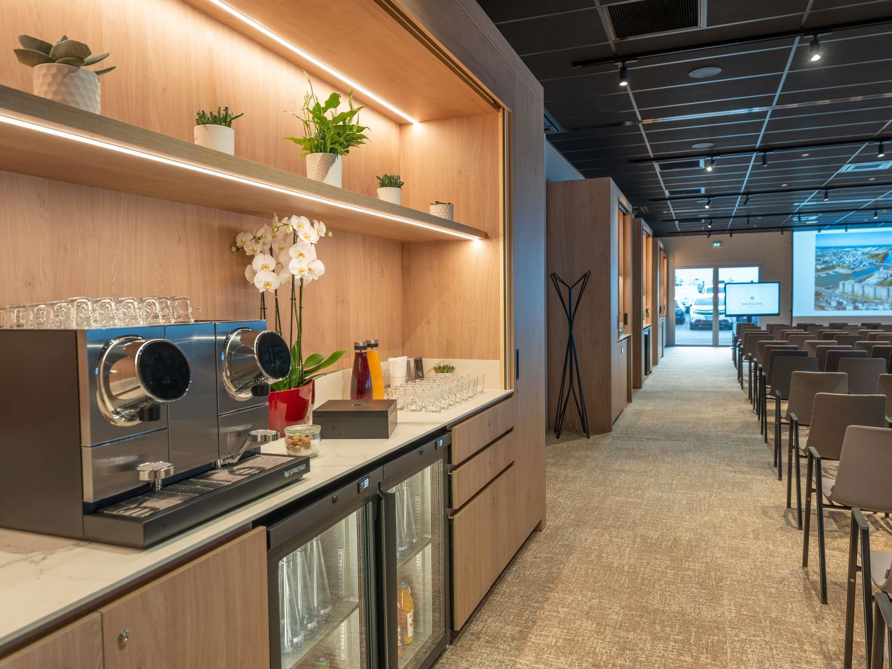 Una cocina moderna con cafetera, refrigerador y encimera con cristalería y una planta.