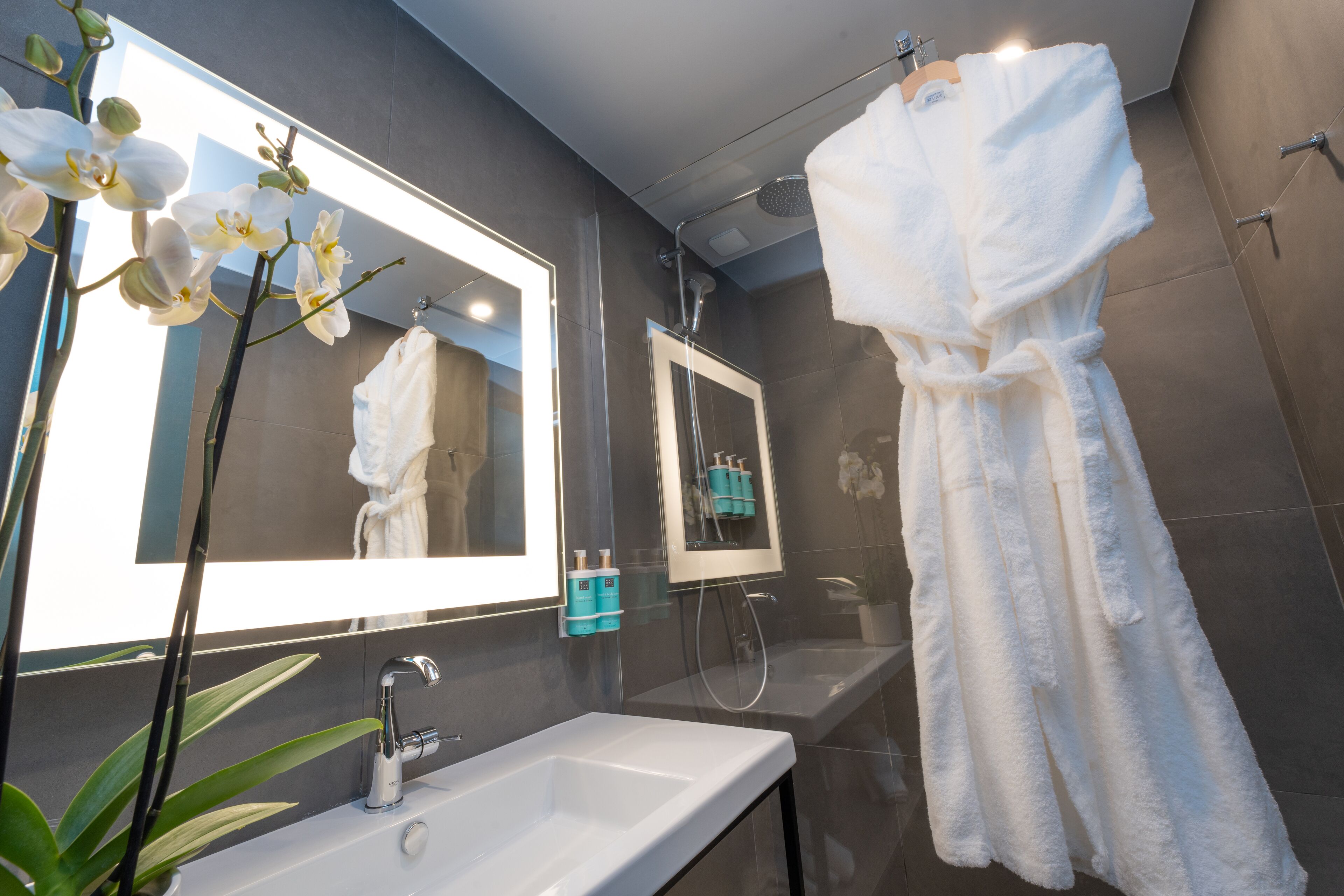 A modern bathroom with a large mirror, white sink, and a shower area.