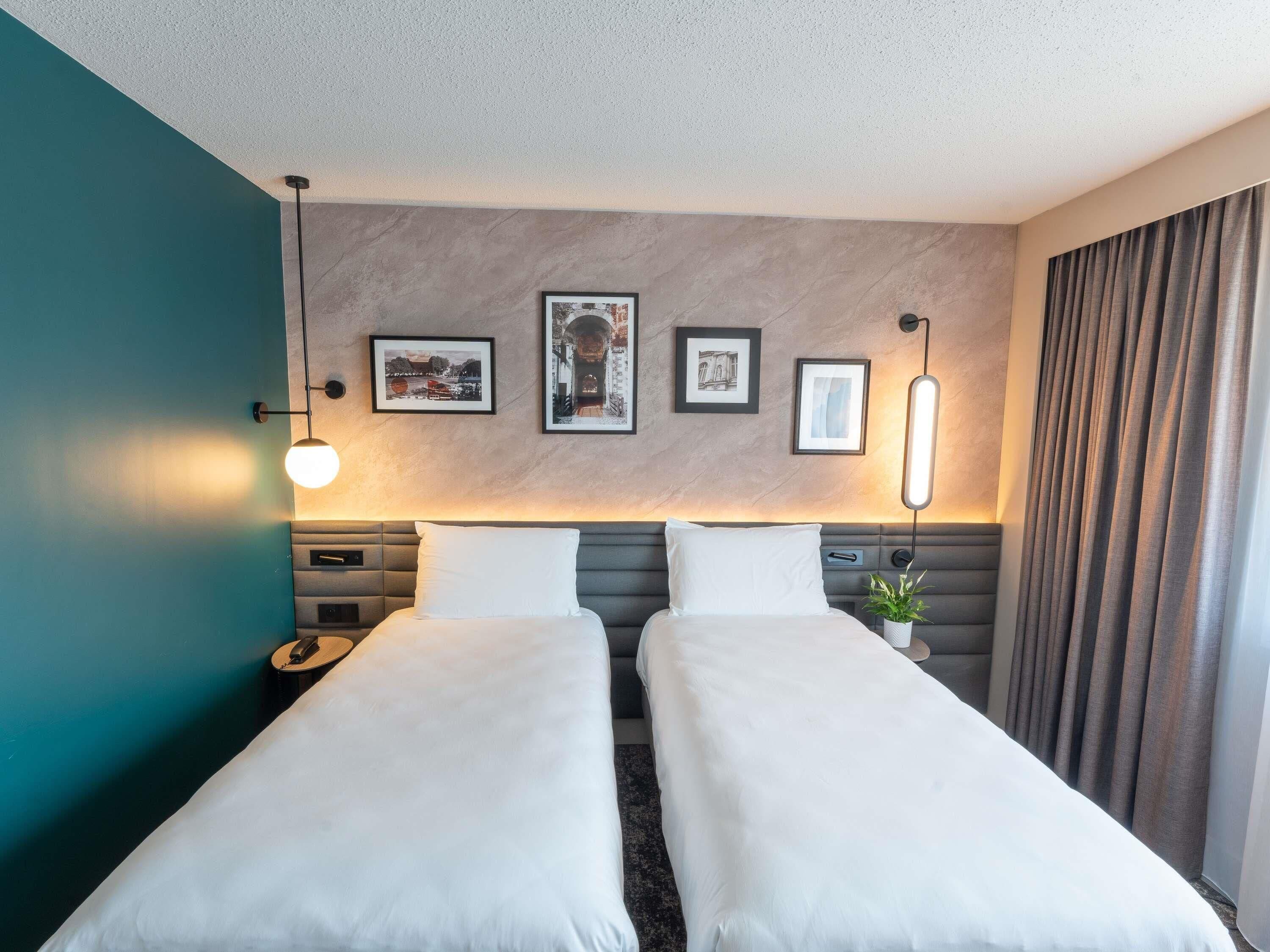 Une chambre d’hôtel avec deux lits, un mur d’accent de couleur turquoise et des tableaux encadrés au-dessus de la tête de lit.