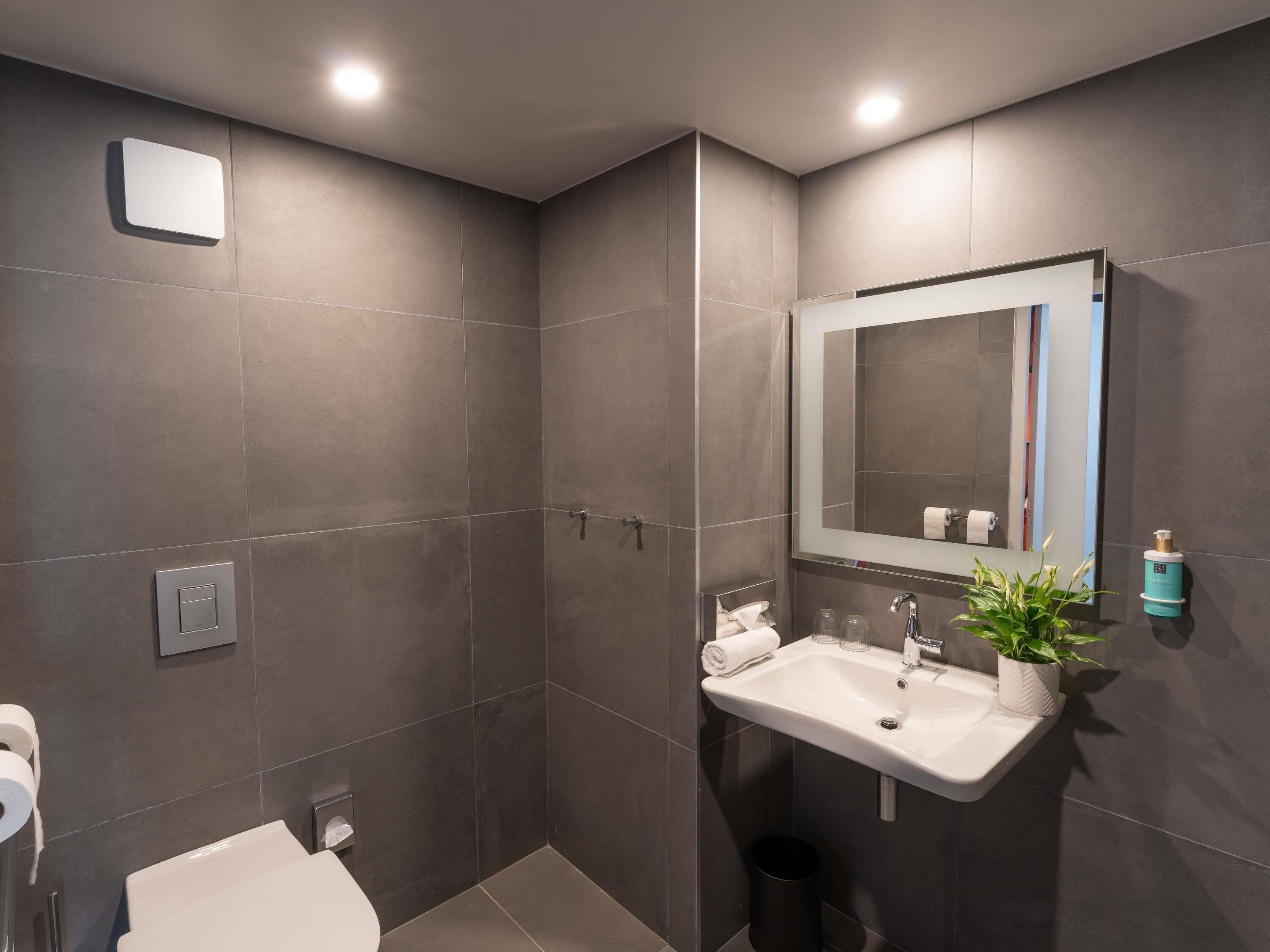 Un baño moderno con inodoro, lavabo, espejo y ducha.