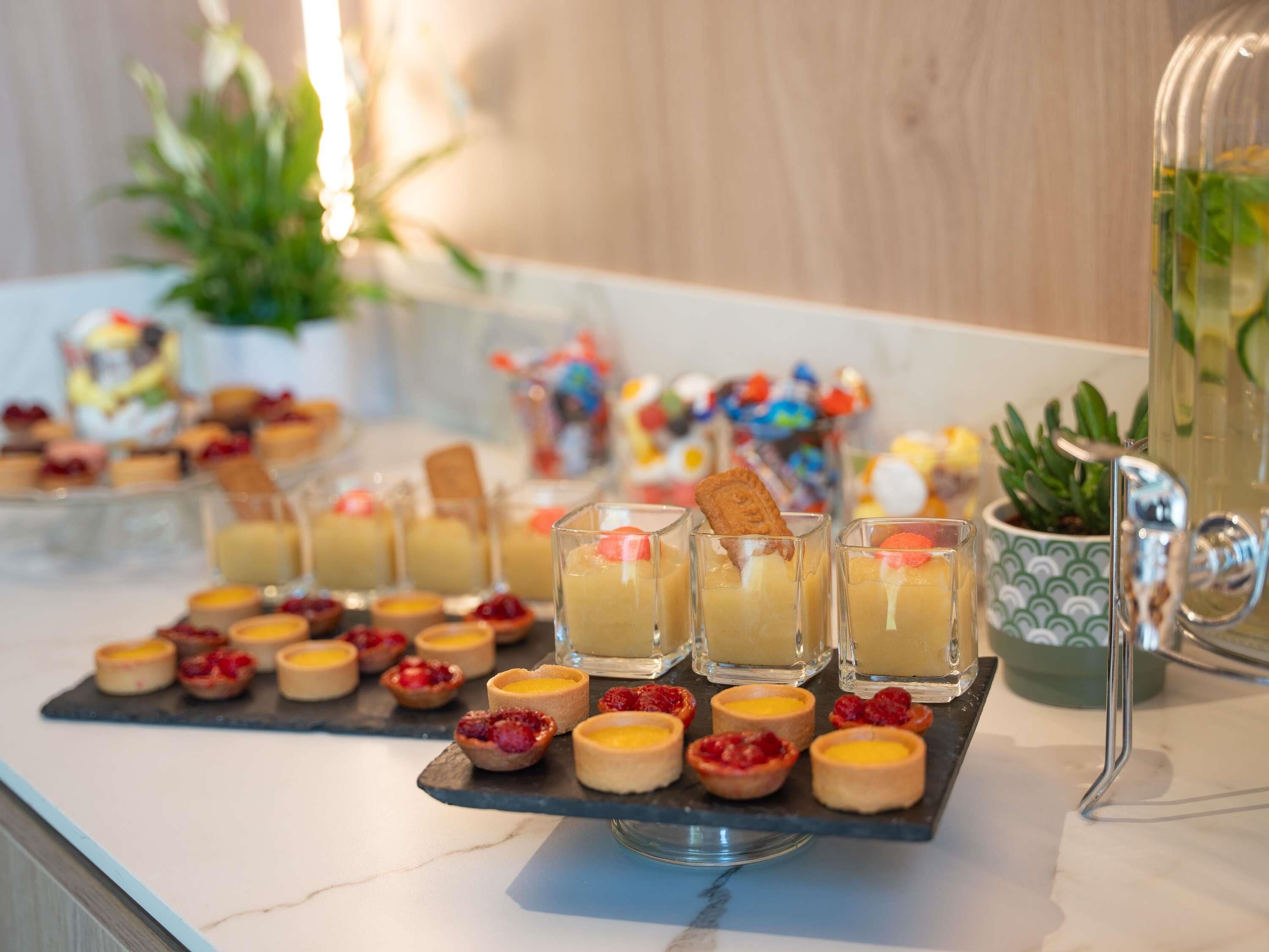A dessert table with various pastries and small cakes, including tarts and custard cups, arranged on a slate board.