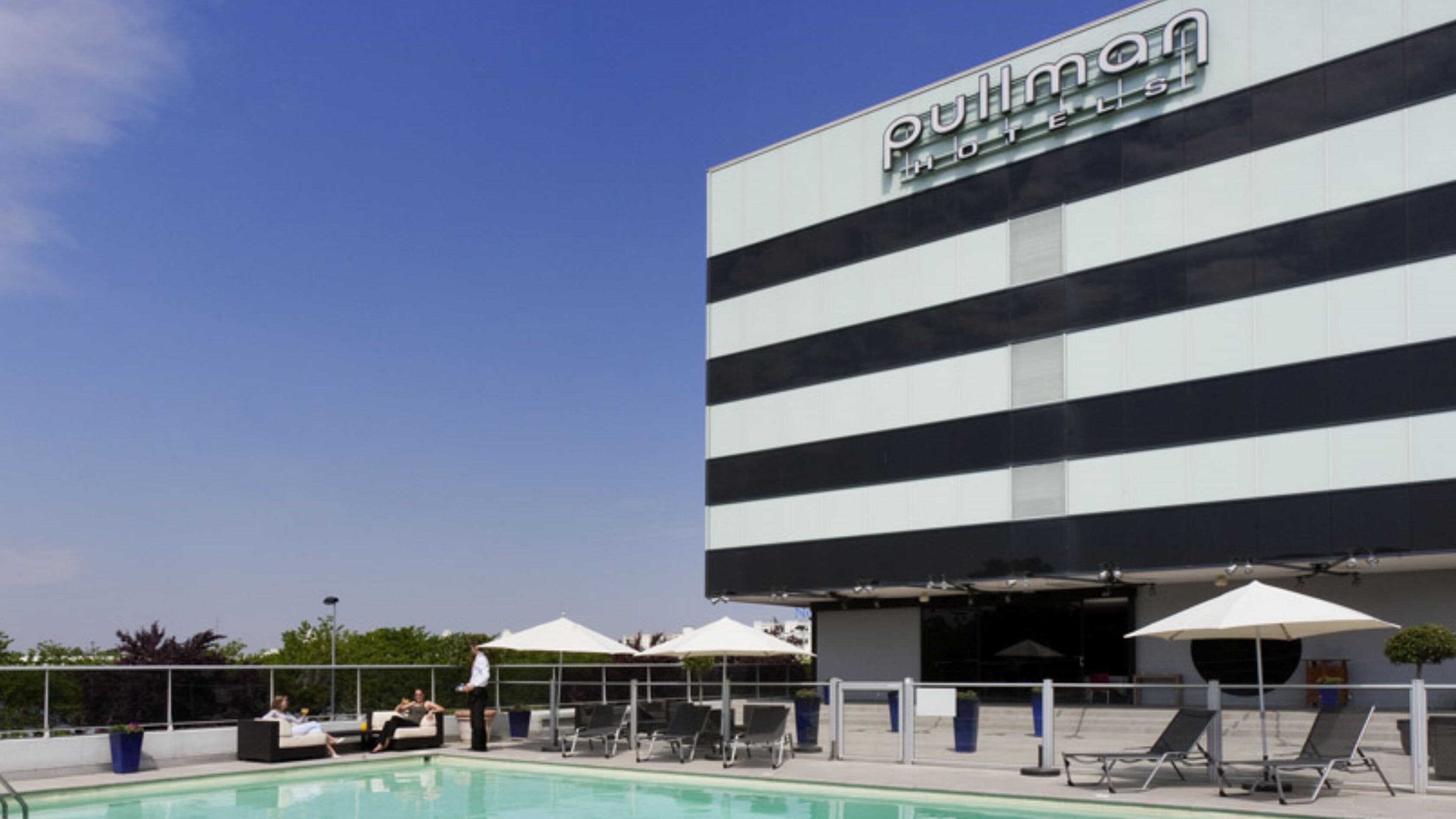 Un hotel con piscina, sillas de descanso y sombrillas.