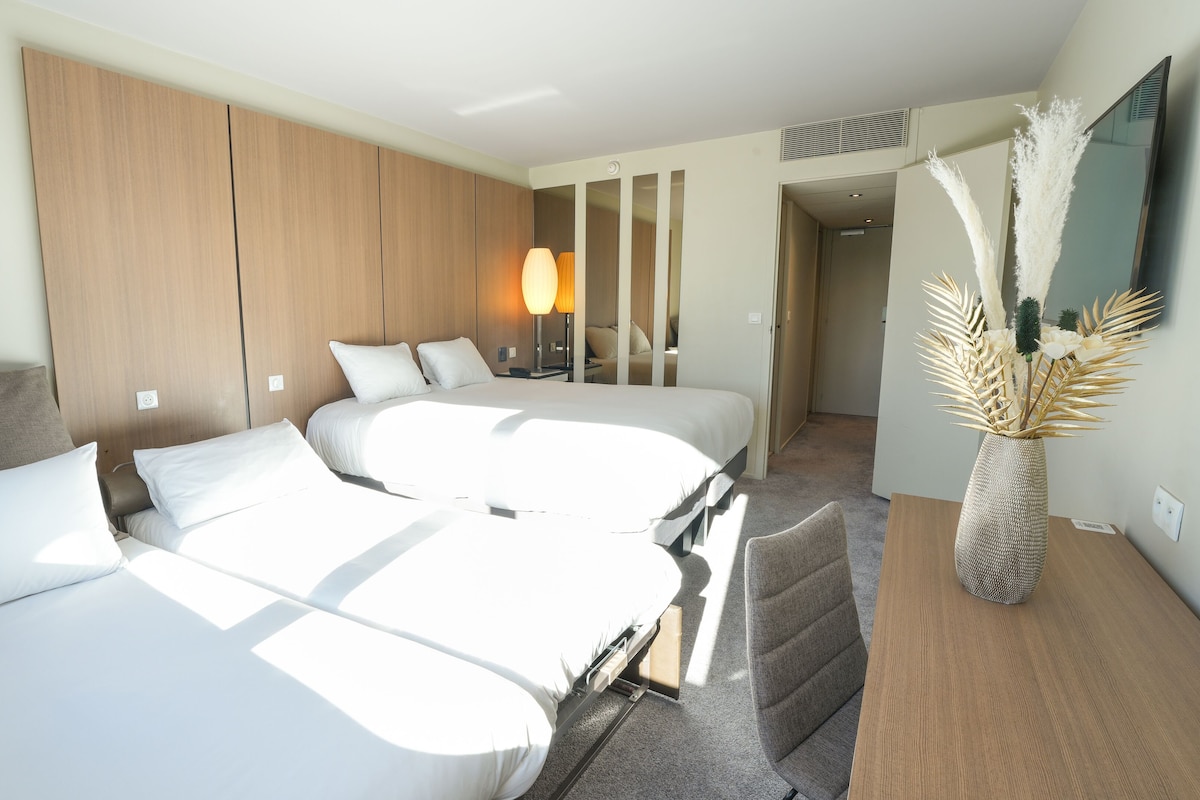 Habitación de hotel con dos camas, cabecero de madera, lámpara, espejo y un florero decorativo.
