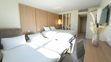 Habitación de hotel con dos camas, cabecero de madera, lámpara, espejo y un florero decorativo.