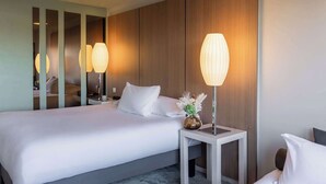 A hotel room with a large bed, two bedside tables, a nightstand, and a mirror. - Hotel Pullman Bordeaux Lac (Bordeaux)