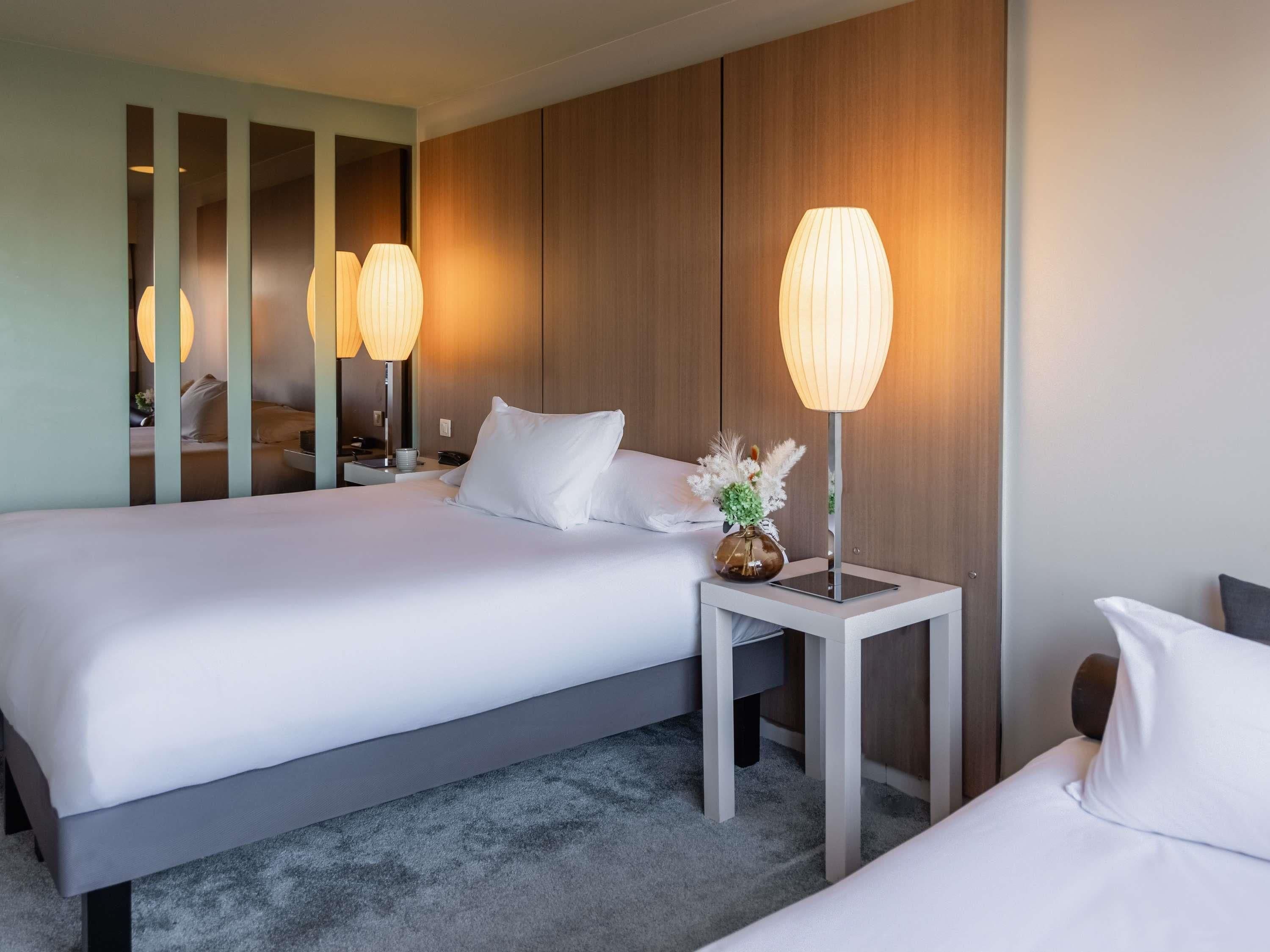 Una habitación de hotel con una cama grande, mesitas de noche, un espejo y una lámpara.