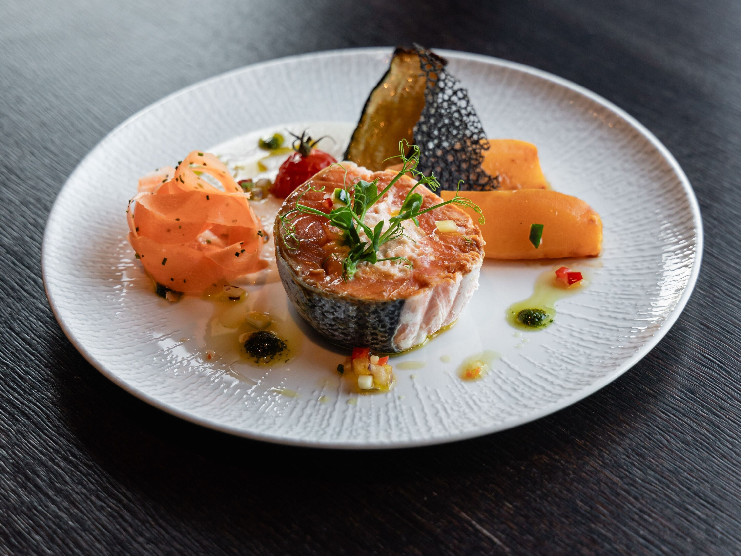 A plate of food with various dishes including salmon, a fish cake, and vegetables.