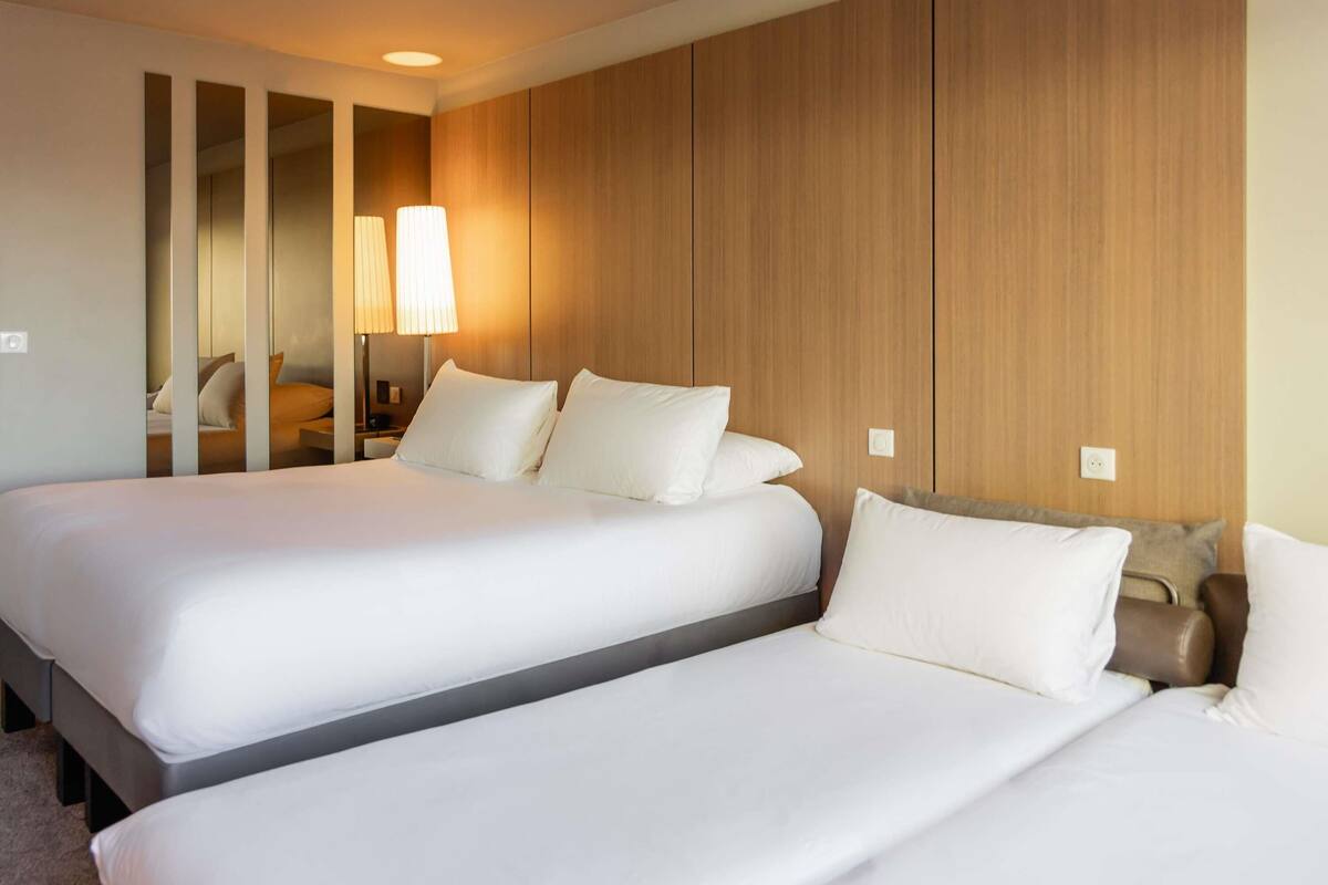 A hotel room with two beds, a wooden panel wall, a nightstand, and a lamp.
