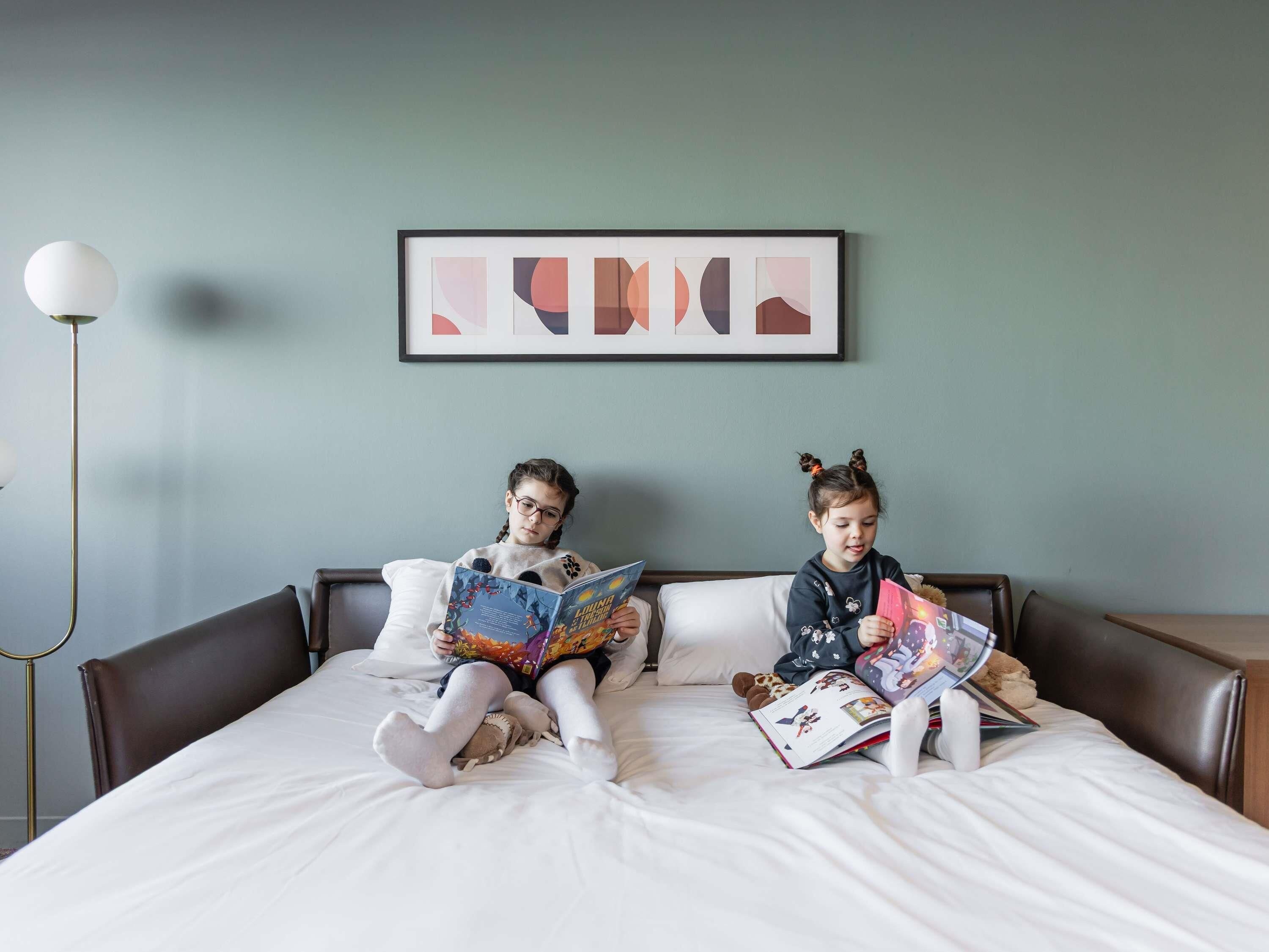 Two children reading on a bed with a framed abstract painting above.