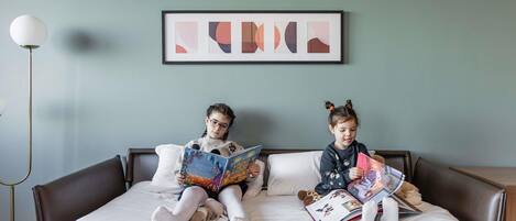 Two children reading on a bed with a framed abstract painting above.