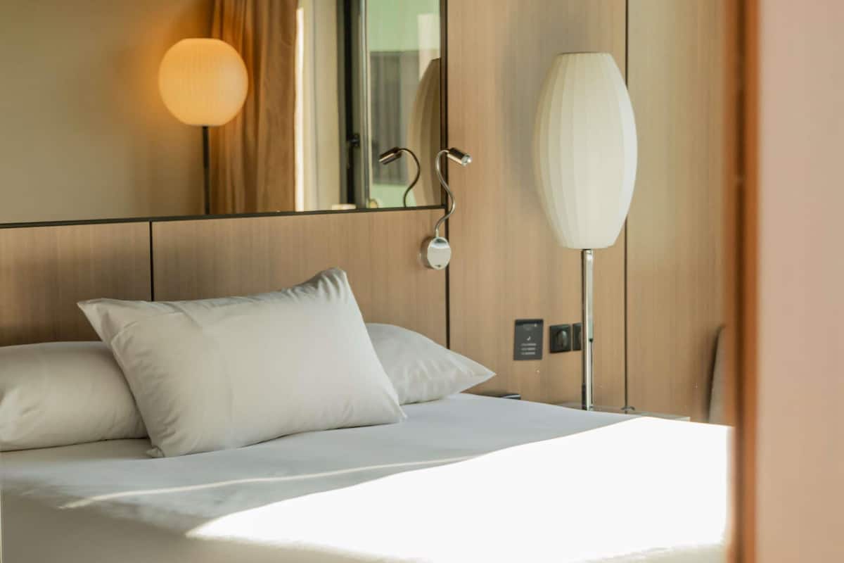 Une chambre d’hôtel avec un lit, une table de chevet, une lampe et un miroir.