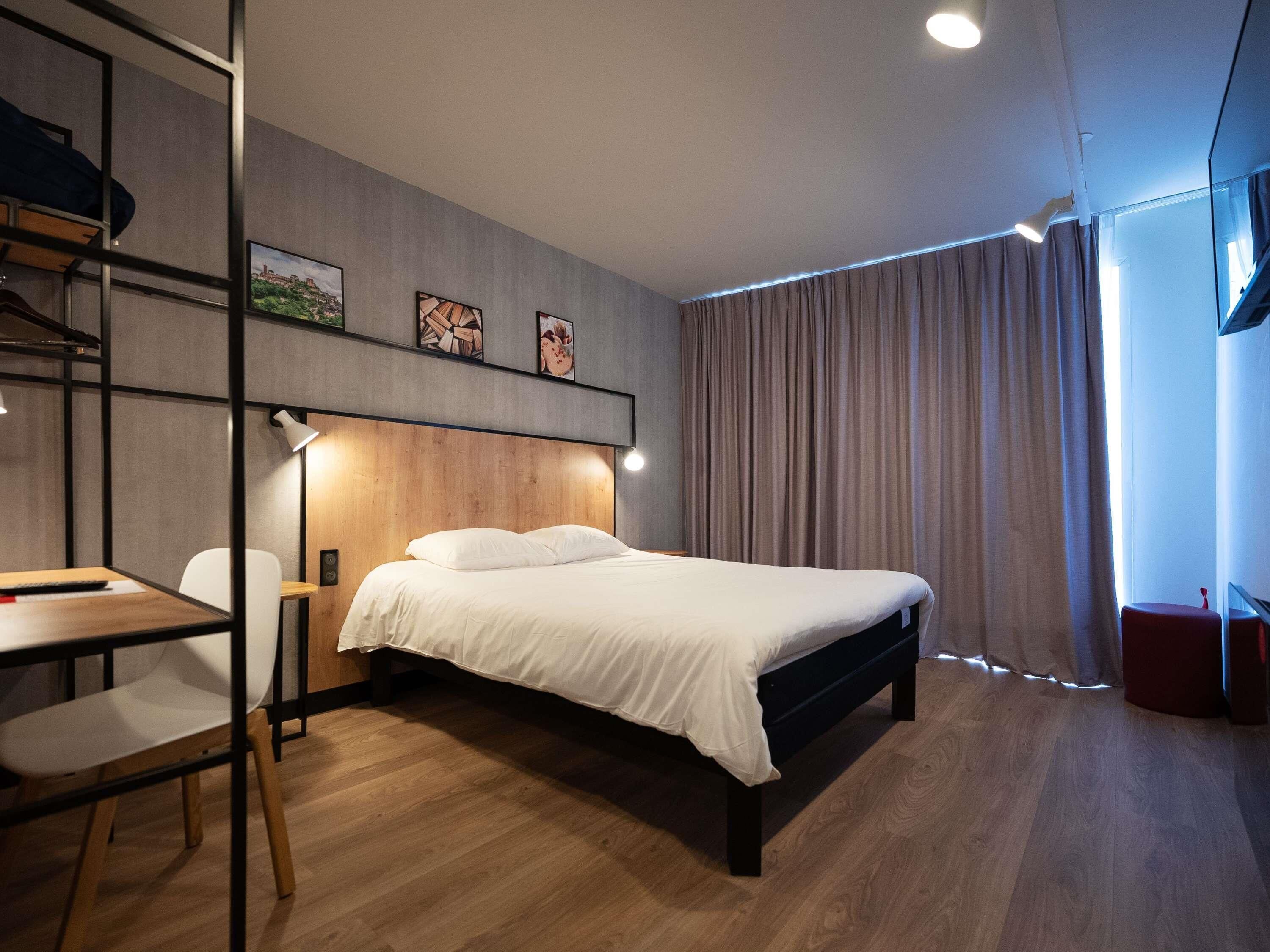 A modern bedroom with a bed, desk, chair, and artwork on the wall.