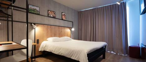 A modern bedroom with a bed, desk, chair, and artwork on the wall.