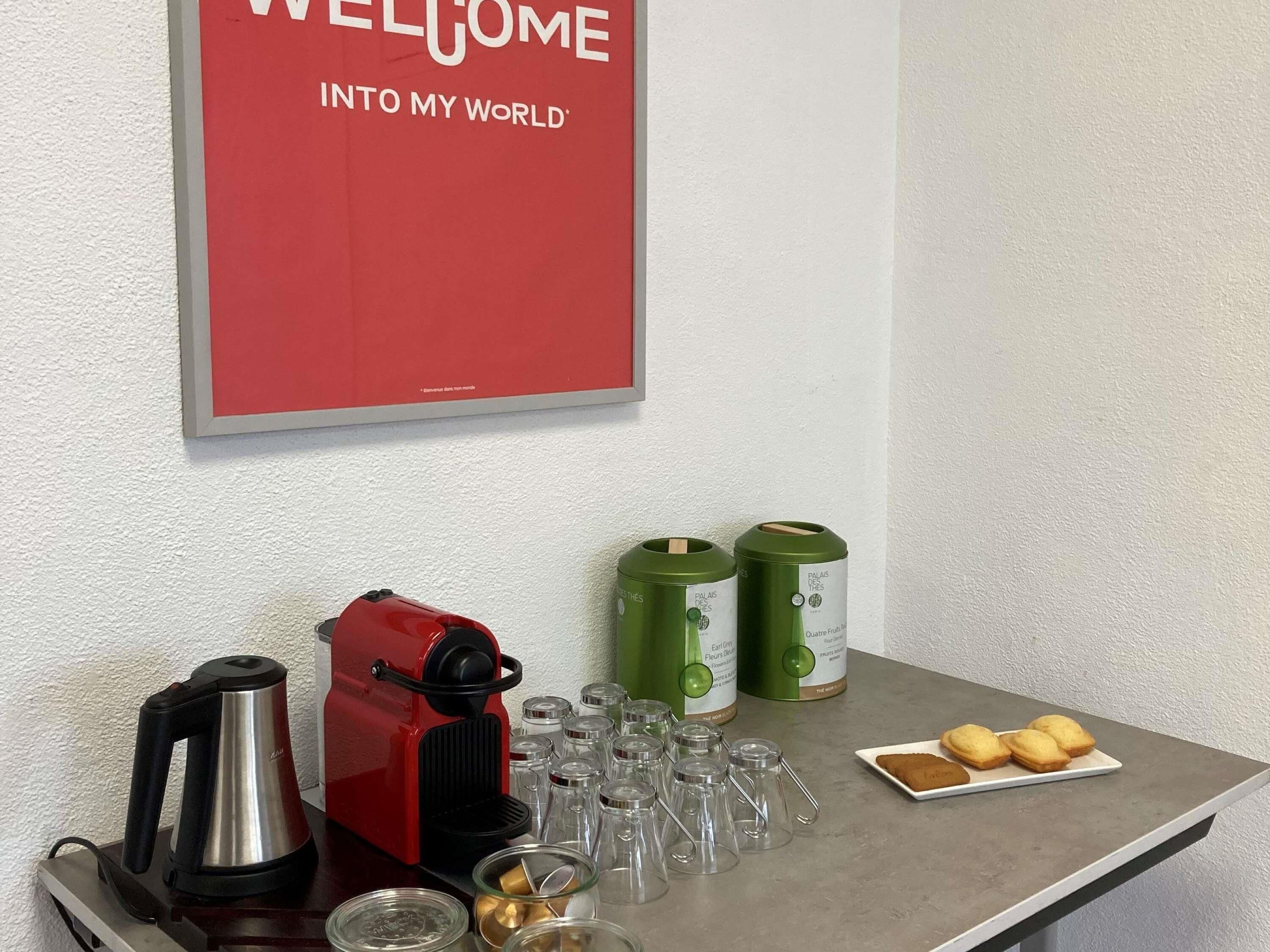Una encimera de cocina con una cafetera roja, dos botes de basura verdes y un letrero de bienvenida.