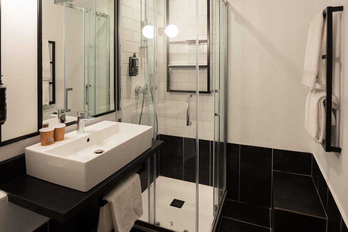A modern bathroom with a glass-enclosed shower, a white sink, and a black countertop.