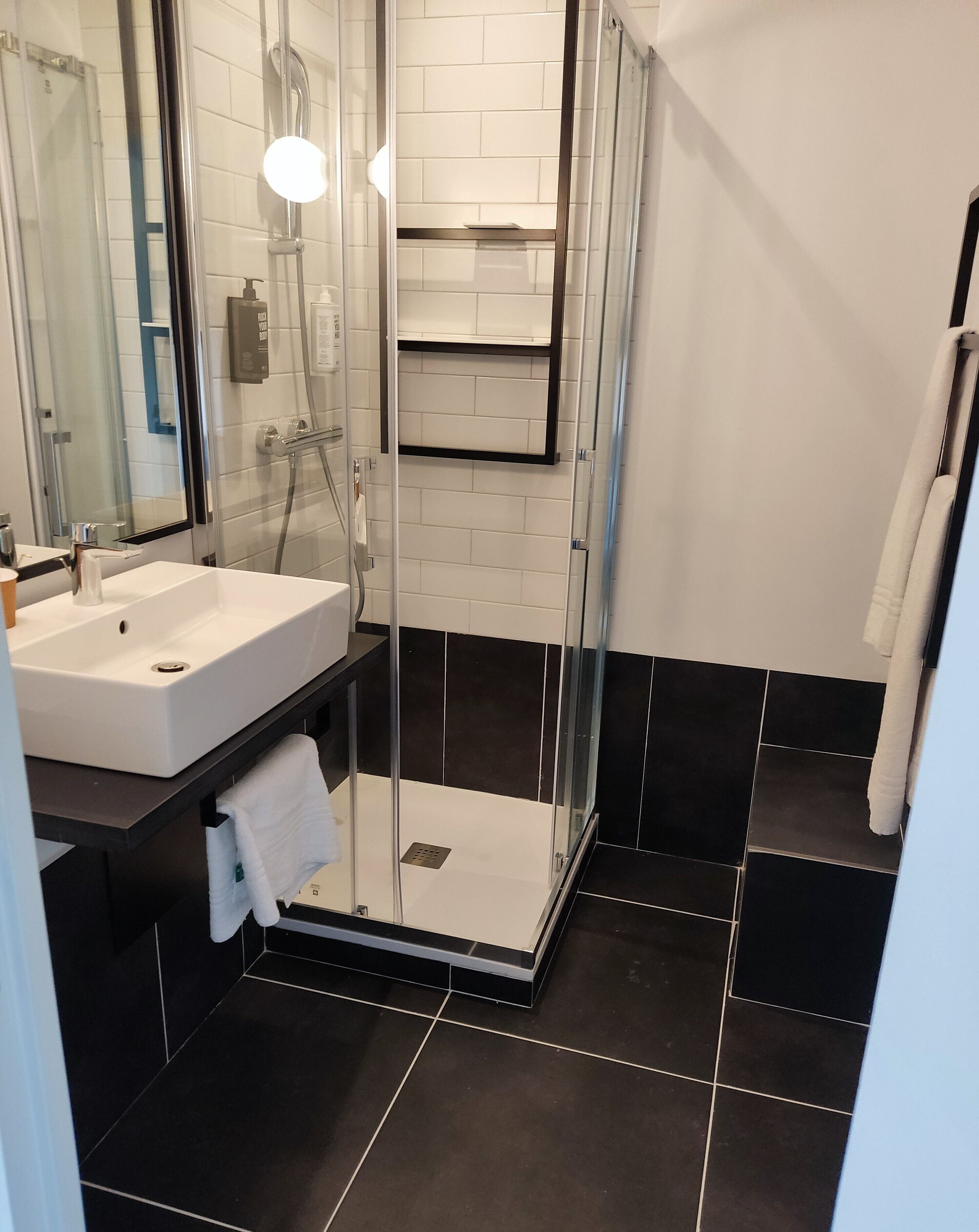 A modern bathroom with a glass-enclosed shower, a white sink, and black-tiled flooring.